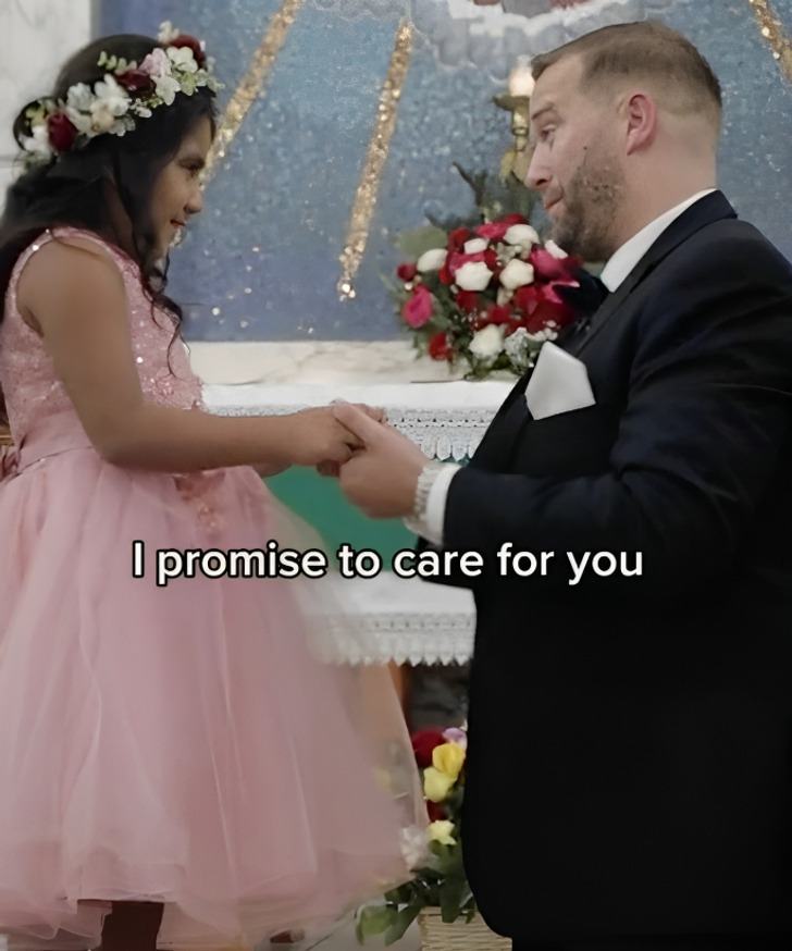 A man wearing a black suit is on his knees while holding a girl's hands.